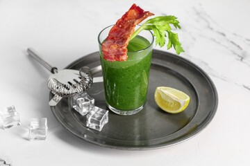 Glass of green bloody mary cocktail with bacon, celery and lime on white background, closeup