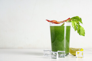 Glass of green bloody mary cocktail with bacon, celery and lime on white background