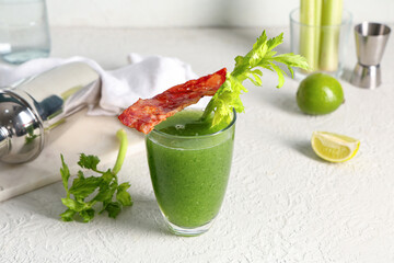 Glass of green bloody mary cocktail with bacon, celery and lime on white background, closeup