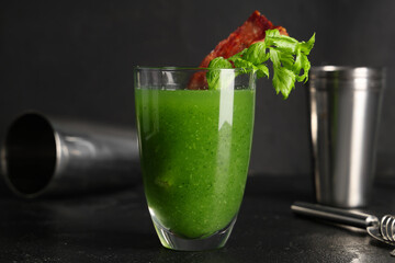 Glass of green bloody mary cocktail with bacon and celery on black background