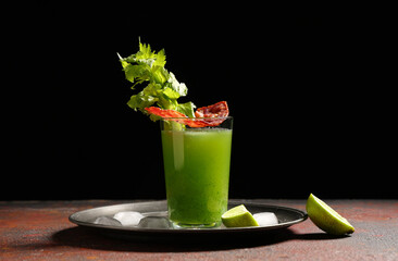 Glass of green bloody mary cocktail with bacon, celery and lime dark table against black background