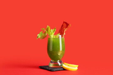 Glass of green bloody mary cocktail with bacon, celery and lemon on red background