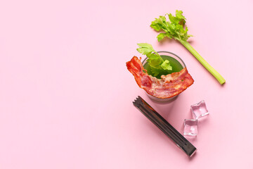Glass of green bloody mary cocktail with bacon, celery and ice cubes on pink background