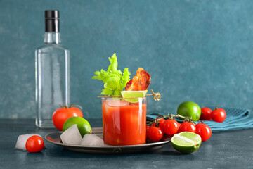 Glass of bloody mary cocktail with bacon, celery and lime on blue background