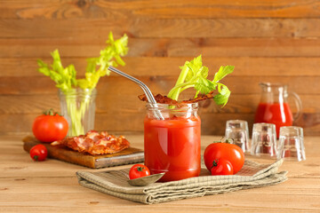 Mason jar of bloody mary cocktail with bacon and celery on wooden background