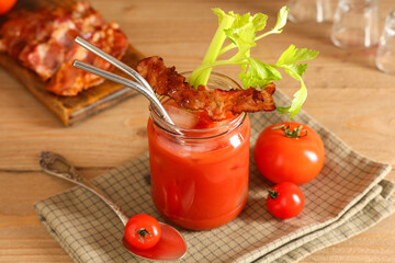 Mason jar of bloody mary cocktail with bacon and celery on wooden background, closeup