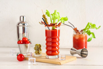Glass of bloody mary cocktail with bacon, celery and olives on white background
