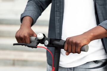 Closeup of african american guy holding handle of a black stand-up scooter, blurred background