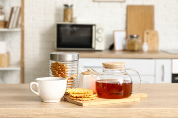 Teapot with jar of waffles and cup on table in kitchen
