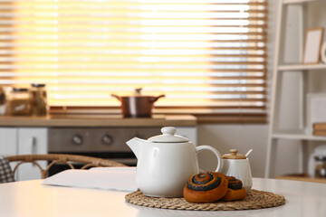 Teapot with tasty poppy buns and jar of sugar on table in kitchen