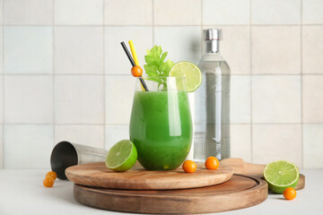 Glass of green bloody mary cocktail with physalis berries and lime on white table