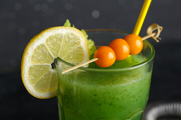 Glass of green bloody mary cocktail garnished with physalis berries and lemon on black background,...