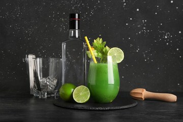 Glass of green bloody mary cocktail garnished with lime, physalis berry and cucumber slice on black background