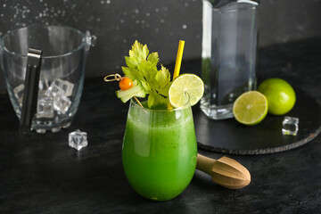 Glass of green bloody mary cocktail garnished with lime, physalis berry and cucumber slice on black...