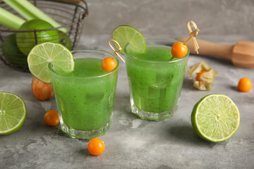 Glasses of green bloody mary cocktail garnished with physalis berries and lime on grey background