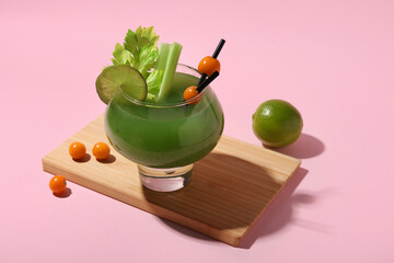 Glass of green bloody mary cocktail garnished with physalis berries and lime on pink background