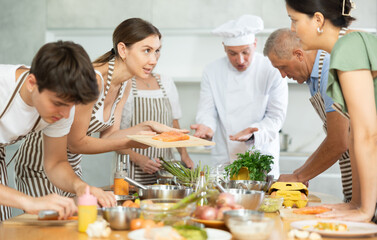 Friendly smiling young woman talking to culinary enthusiasts during group cooking masterclass from professional chef..