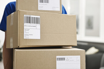 Man holding parcels with shipping labels indoors, closeup