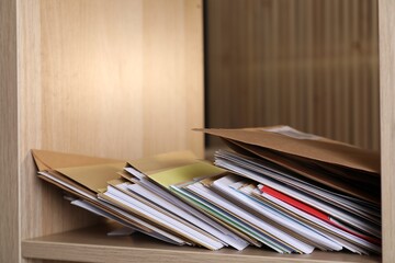 Different paper envelopes on wooden shelf in post office, closeup