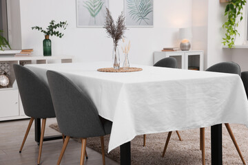 Table with white tablecloth, dried flowers in vases and chairs in stylish room. Interior design
