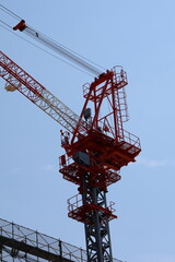 A large construction crane with a long, angled arm extending into the sky. Cables, pulleys, and a platform with ladders are visible, indicating an industrial or construct
