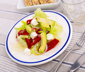 Fresh lettuce with red bell peppers, avocado, onions and cheese on a plate. Appetizing salad with vegetables and feta cheese. Delicious and healthy food