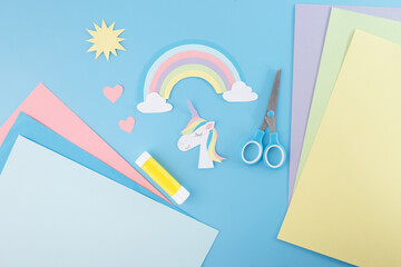 Paper crafting scene with unicorn, rainbow, Includes scissors, glue, and colored paper sheets....