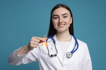 Multiple Sclerosis awareness. Happy doctor holding orange ribbon on light blue background