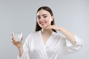 Happy woman with glass of collagen water on grey background