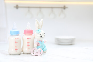 Feeding bottles with baby formula, pacifier and toy bunny on white table indoors. Space for text