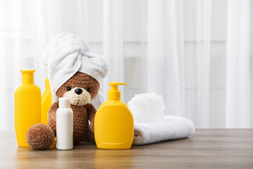 Baby cosmetic products, shower puff and toy bear with towel on wooden table indoors. Space for text