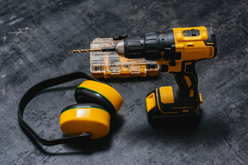 Yellow cordless drill drill with ear protection and bits on dark surface. Powerful tool for construction and DIY projects.