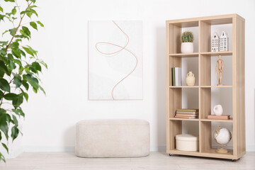 Shelving unit with different home decor, houseplant and ottoman near white wall indoors