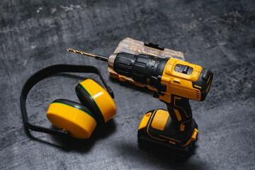 Fototapeta premium Yellow cordless drill drill with ear protection and bits on dark surface. Powerful tool for construction and DIY projects.