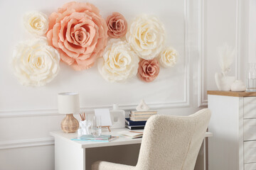 Beautiful decorative paper flowers on white wall and stylish furniture indoors