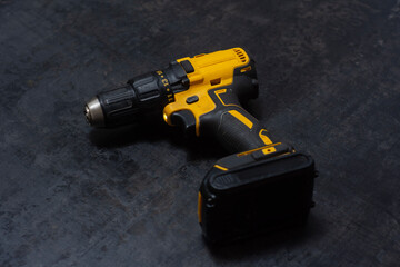 Yellow cordless drill rests on a dark textured surface. Powerful tool for construction and DIY projects.