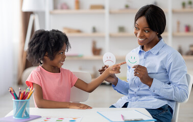 Female teacher friendly pretty young black woman and little girl preschooler exercising at daycare,...