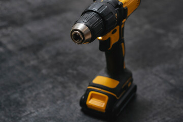 Yellow cordless drill rests on a dark textured surface. Powerful tool for construction and DIY projects.