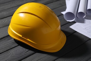 Hard hat and different engineering drawings on grey wooden table, closeup