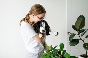 Blonde-haired girl distracted from her tasks, kissing the Spaniel puppy she is holding in her arms