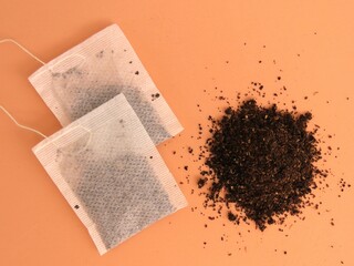 Two tea bags beside a pile of dried tea on orange background.