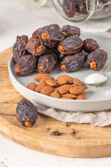 Medjool dates and almonds on a plate with a spoonful of shredded coconut, set on a wooden board with a jar of dates in the background
