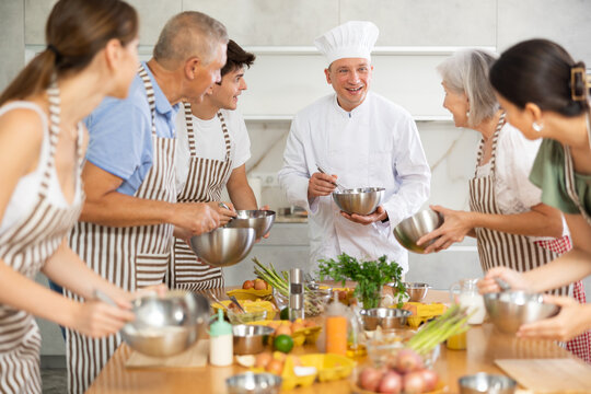 Positive adult man professional chef conducting culinary courses, imparting cooking skills to diverse group of people of different ages..