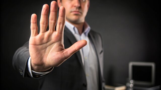 A businessman in a suit raises his hand in a stop gesture, signaling a warning or no entry.
