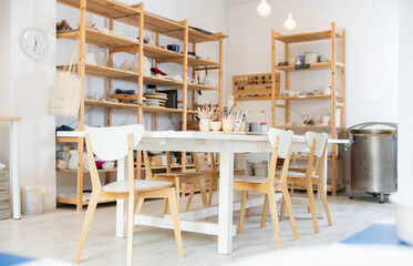 Pottery art studio with wooden shelves and table with necessary tools on it