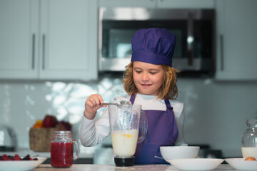 Kid in chef hat and apron. Child chef cook is learning how to make a cake in the home kitchen.