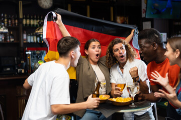 Diverse men and women supporting Germany sports team in pub together. Happy group of friends raising German flag.