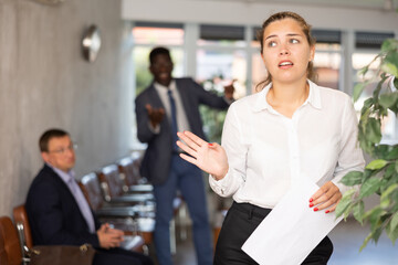 Upset young woman in business clothes posing with documents in her hands at reception