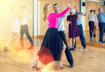 Smiling modern woman and man dancing slow ballroom dance during group class in choreography studio
