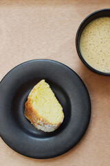 Taza de café capuchino y un trozo de pan dulce sobre una mesa de madera, plano vertical.